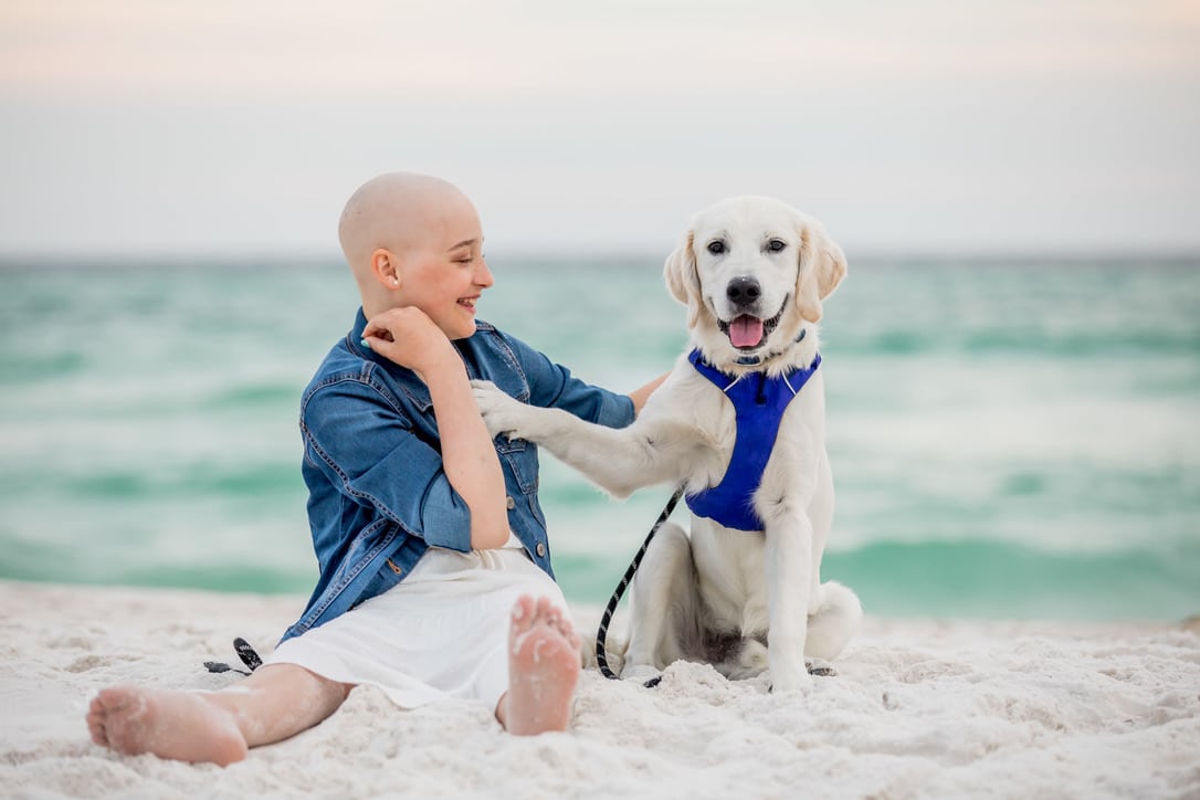 Izzy and Blu sit together on a beach, both are smiling.