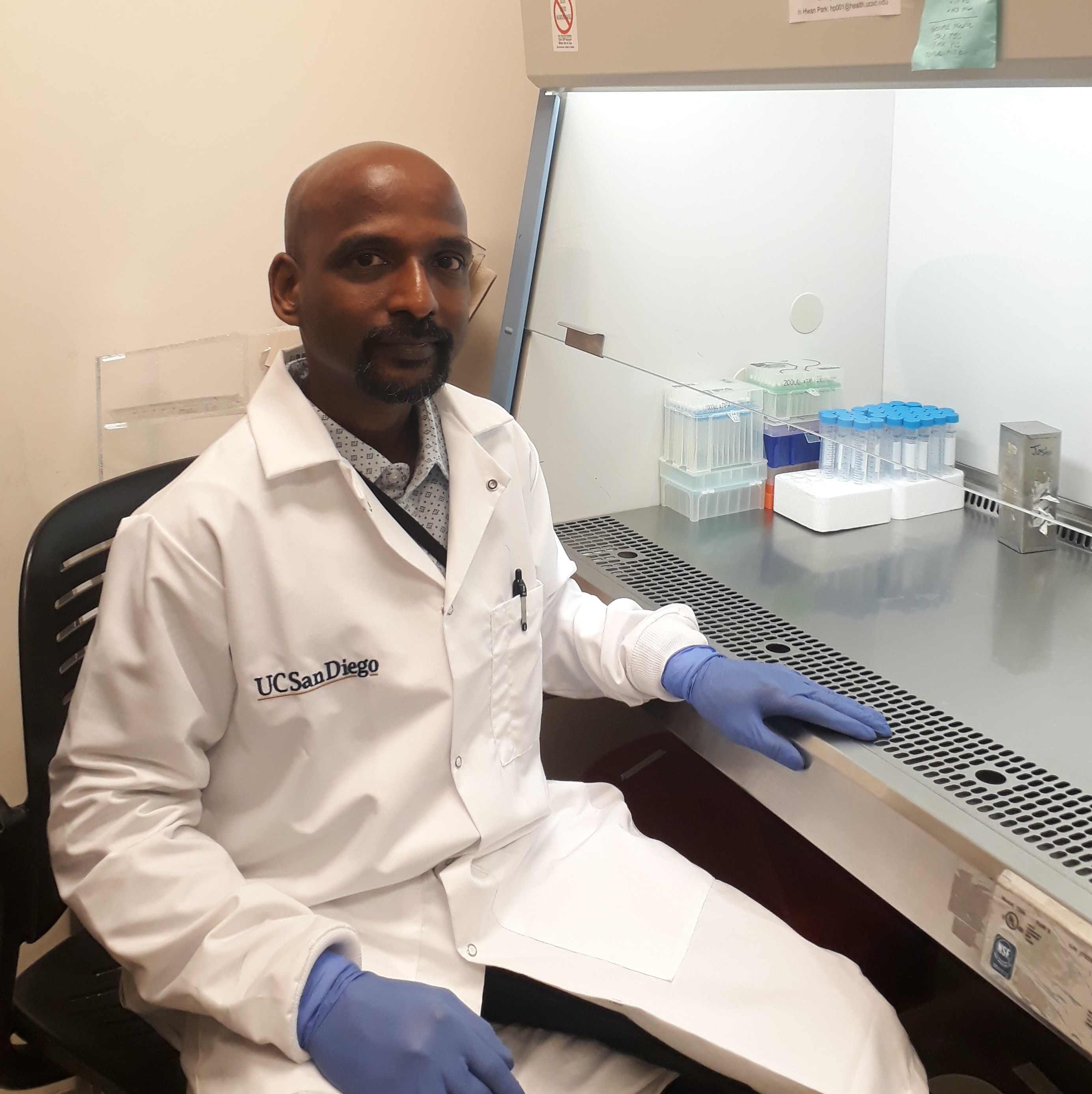 Suresh Madheswaran wearing a white lab coat and gloves in his lab