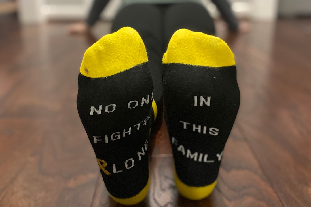 A person wearing black and gold socks that say "No one fights alone in this family."