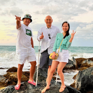 Talgat Omurov (Center), an osteosarcoma survivor, is pictured standing on a beach with his wife and a friend