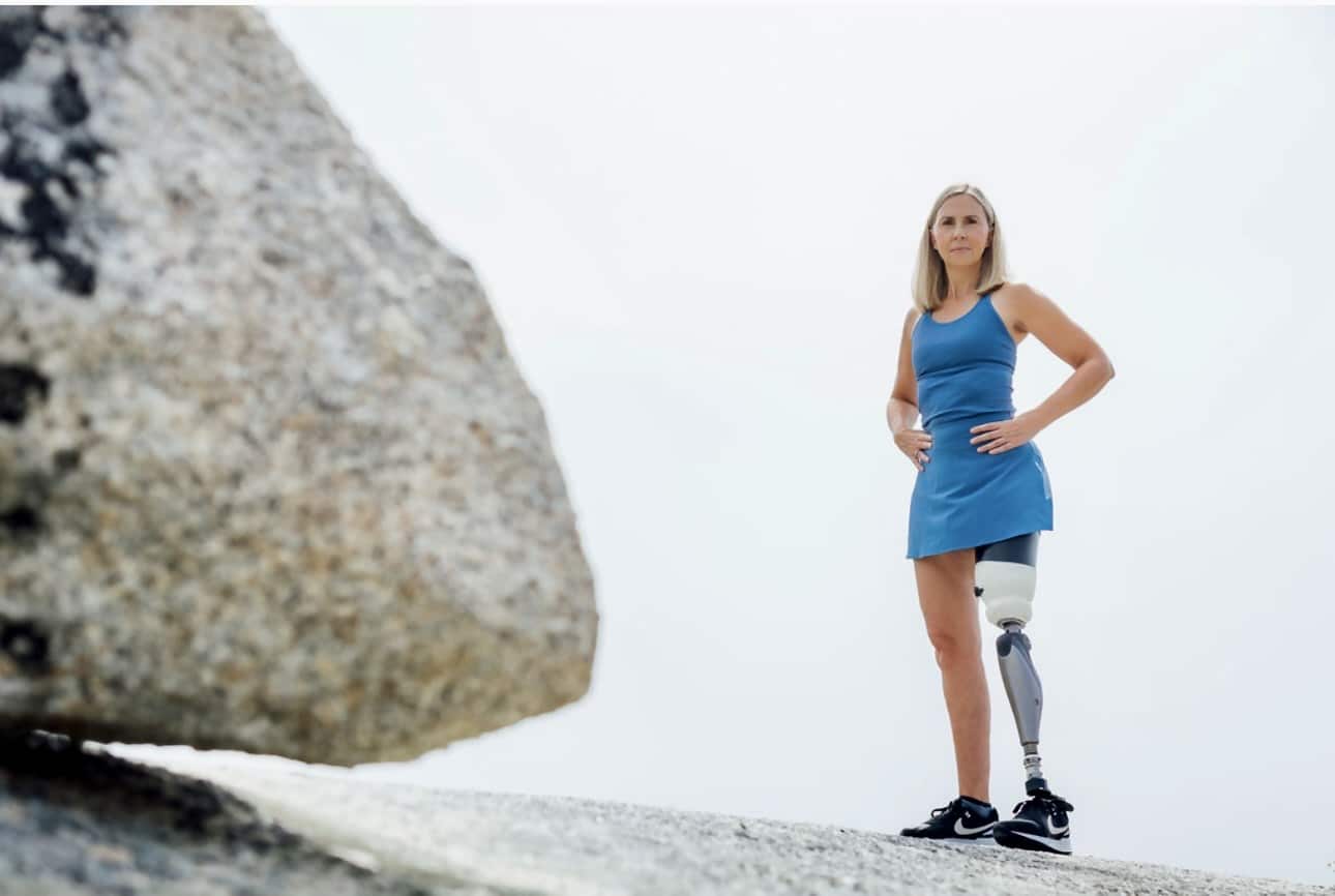 Jill stands next to a boulder and proudly shows off her prosthetic leg.