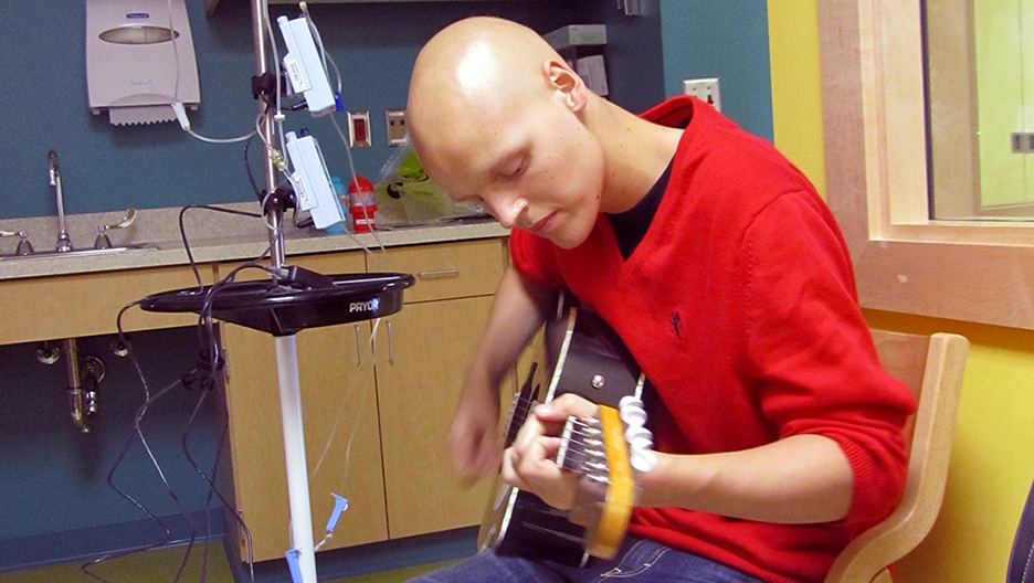 Zach Sobiech plays the guitar in a hospital room.