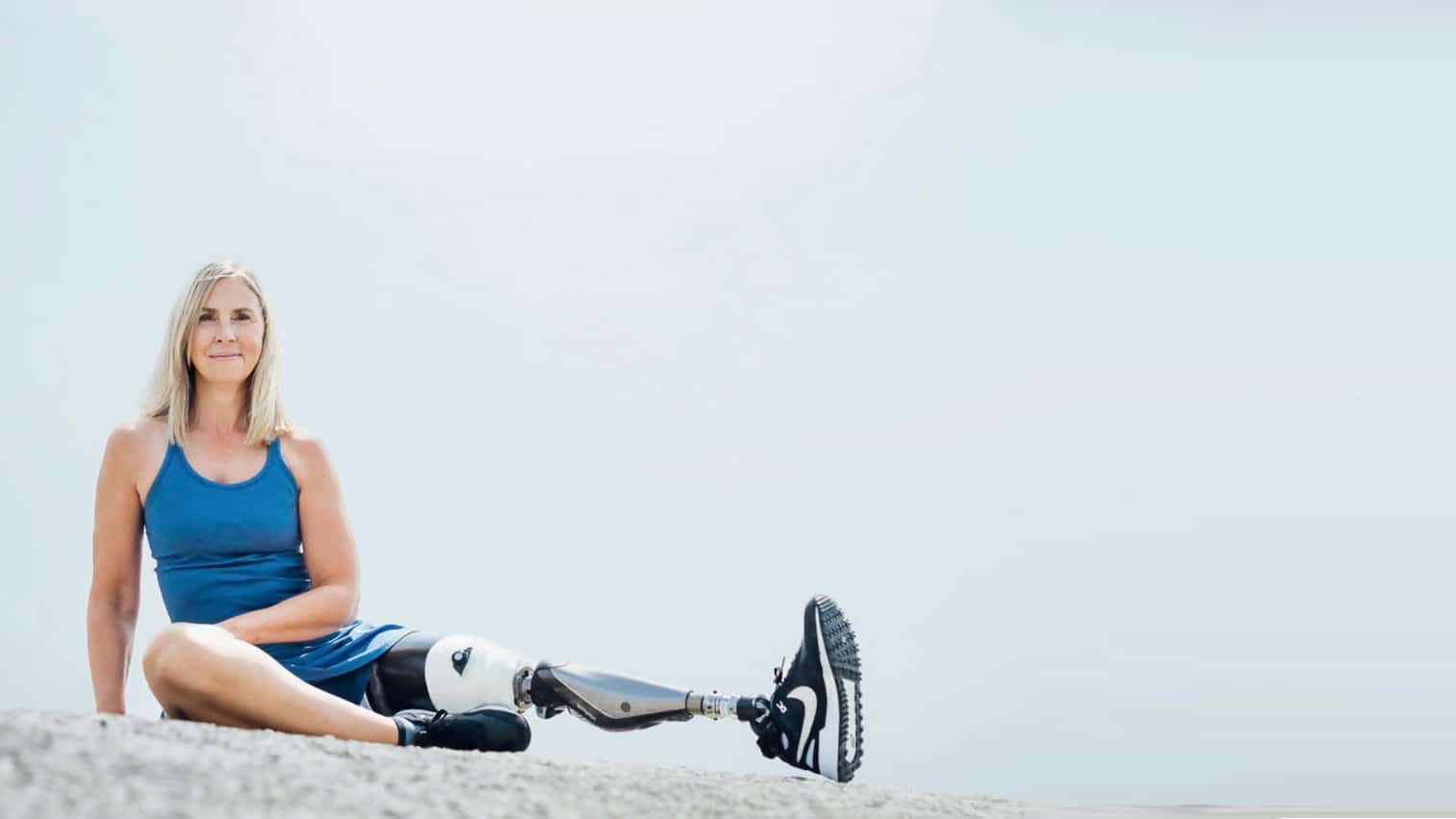 Blonde woman in bright blue dress with a prosthetic leg sitting on top of a boulder