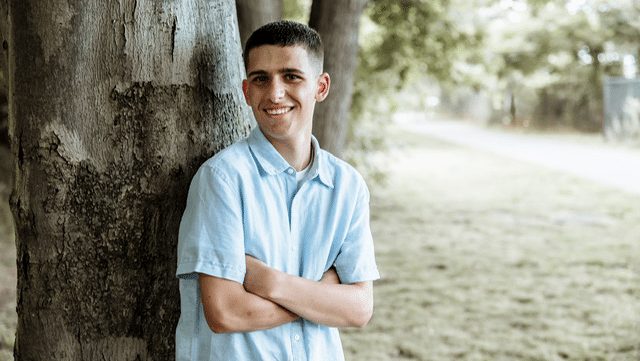 Gavin leaning up against a tree with arms crossed