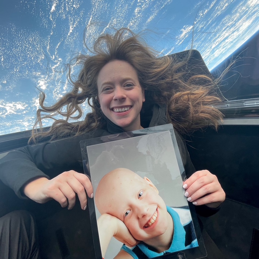 Hayley Arceneaux in space holding a picture of herself as a kid