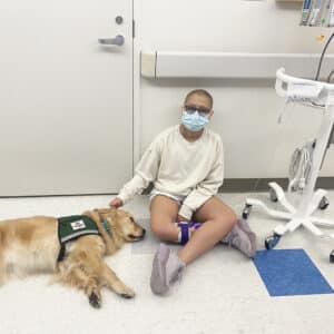 Angie sitting in hospital hallway petting a therapy dog