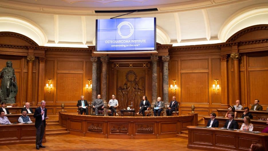 Mac Tichenor gives a speech in a round room with a projector that displays the OSI logo on it
